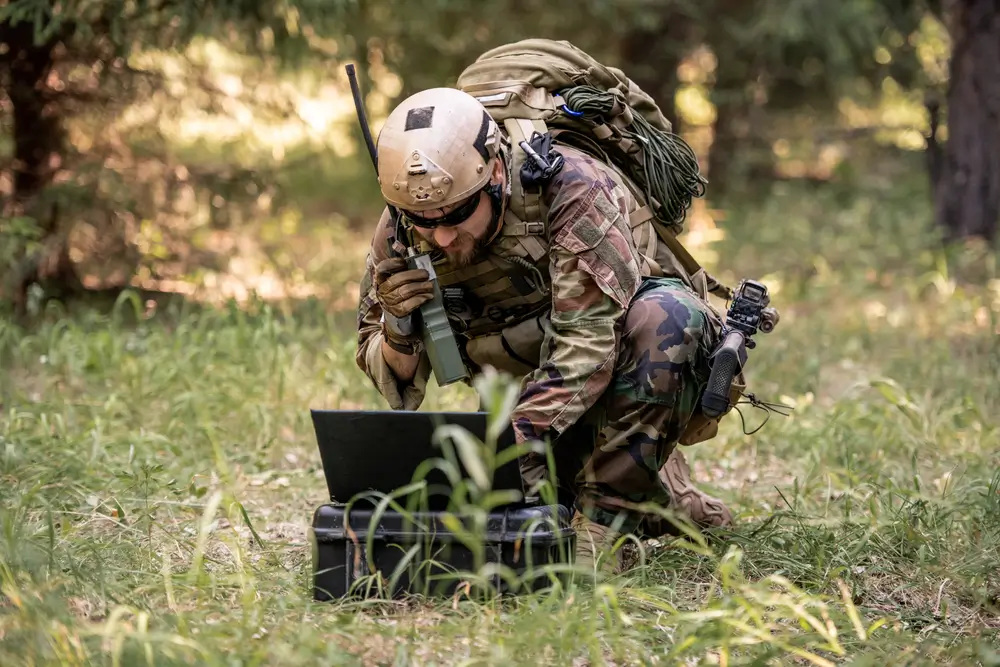 Soldat en opération utilisant une radio militaire vintage en forêt pour assurer des communications claires.