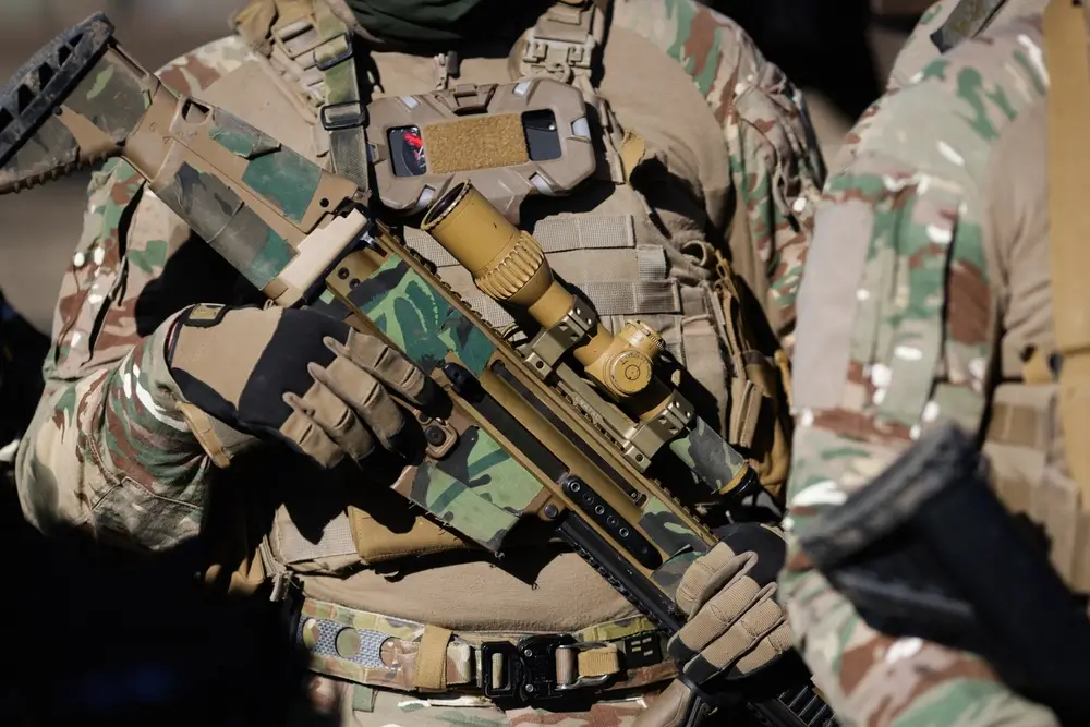 Soldat de l'armée de terre en uniforme de combat avec équipement tactique et fusil de précision camouflé.
