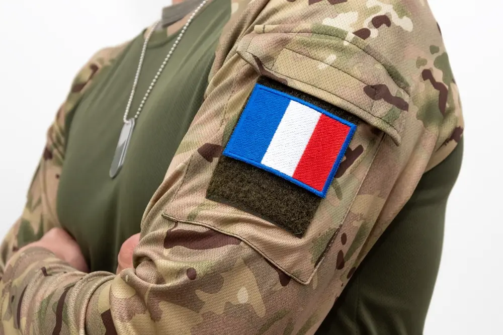 Soldat en uniforme de camouflage portant un insigne militaire du drapeau français sur son épaule.