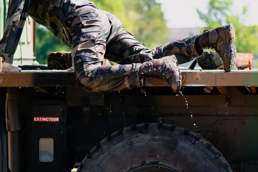 Soldat en treillis camouflé humide grimpant sur un camion lors d'un entraînement militaire sur le terrain.