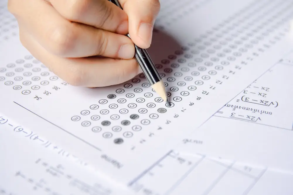 Main d'un candidat remplissant une grille de QCM avec un crayon lors des tests écrits d'un concours militaire.