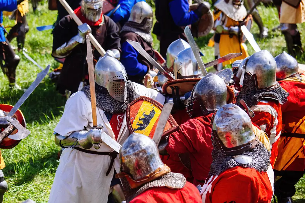 Mêlée de soldats en armure combattant à l'épée sur un champ de bataille médiéval historique en pleine campagne.