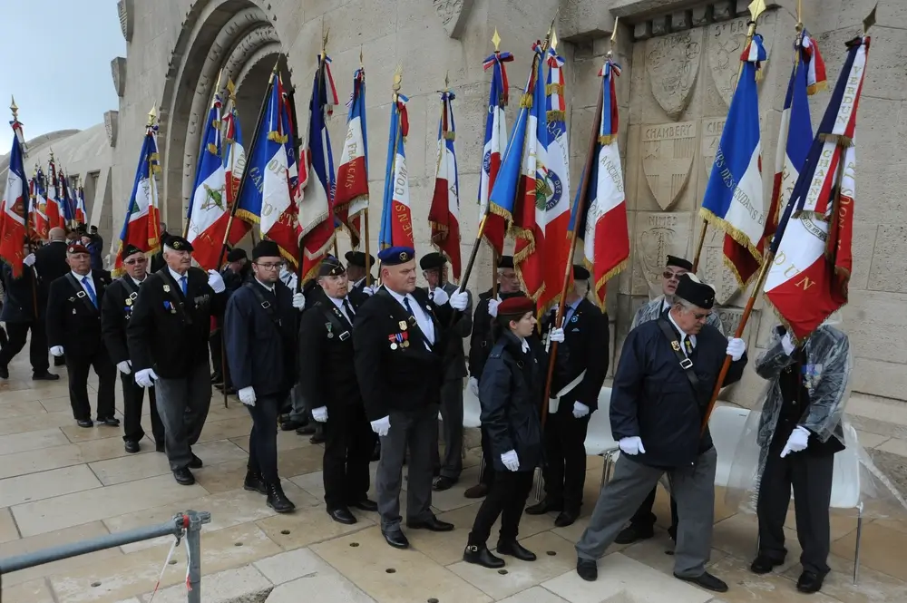 Porte-drapeaux défilant avec des drapeaux tricolores devant un monument en pierre lors d'une cérémonie de recueillement.