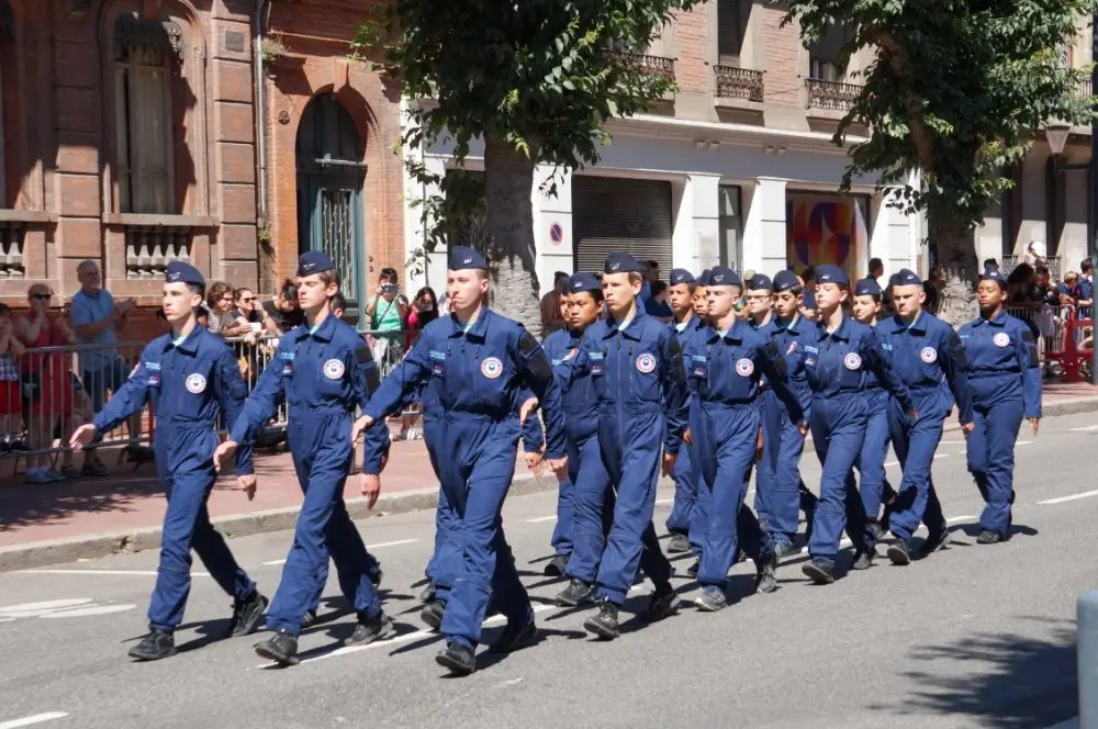 Soldats en marche chantant en cadence lors d'un défilé militaire, perpétuant la tradition du chant régimentaire.