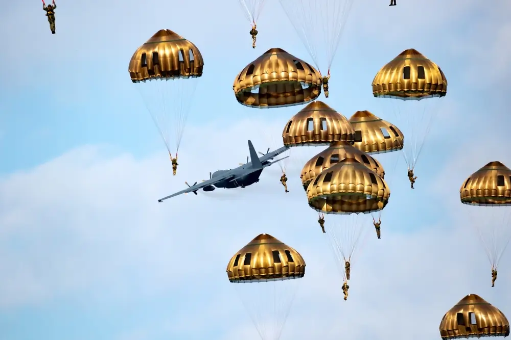 Parachutistes militaires en plein saut groupé, largués depuis un avion de transport tactique dans le ciel.