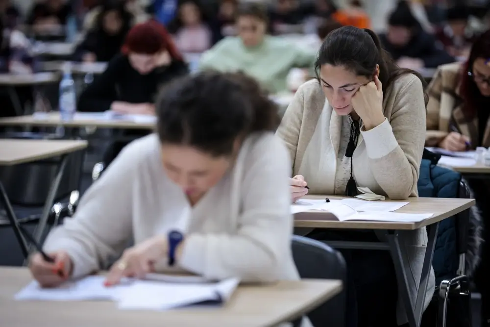 Candidats concentrés rédigeant leur épreuve de culture générale lors d'un concours dans un grand hall d'examen.