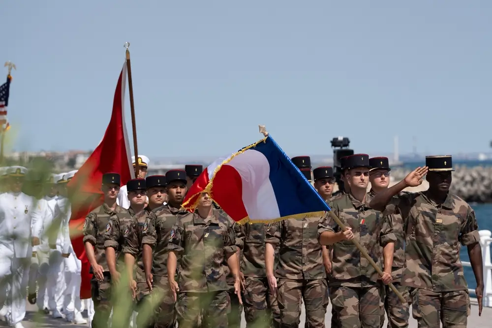 Jeunes stagiaires en tenue camouflée défilant avec le drapeau français lors d'une préparation militaire en régiment.
