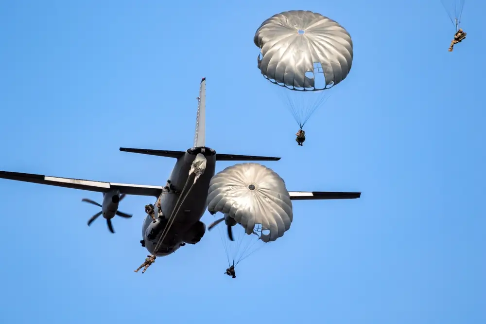 Soldats parachutistes sautant d'un avion de transport militaire, parachutes déployés dans un ciel bleu clair.