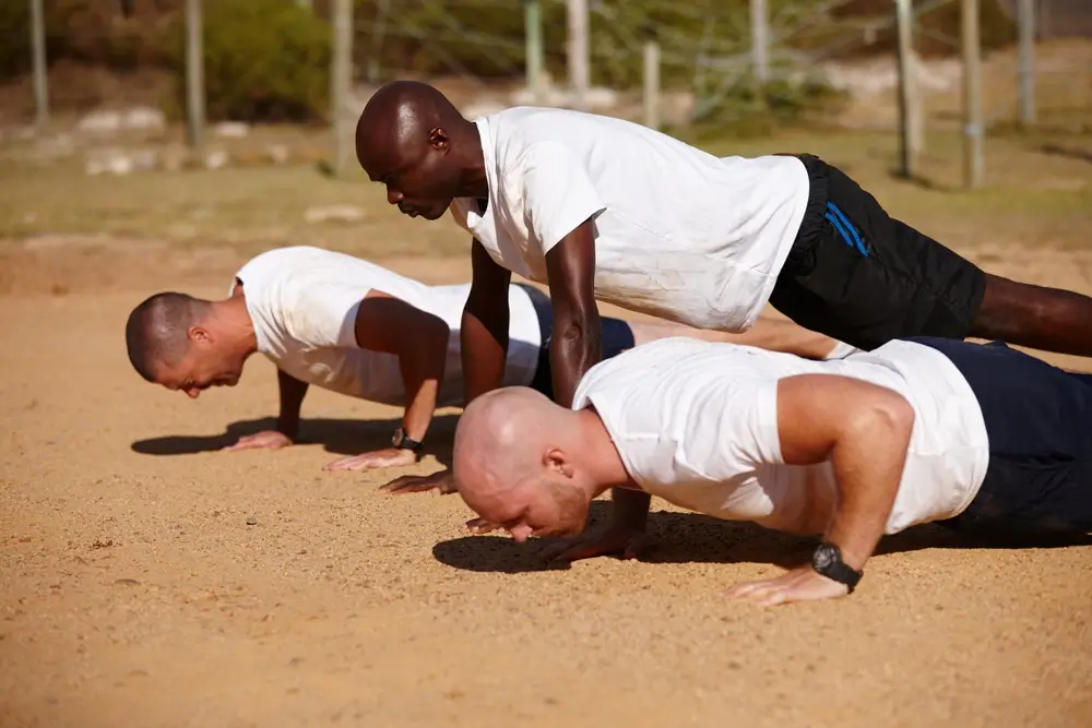 Soldats en t-shirt blanc effectuant des pompes au sol lors d'un entraînement physique militaire en extérieur.