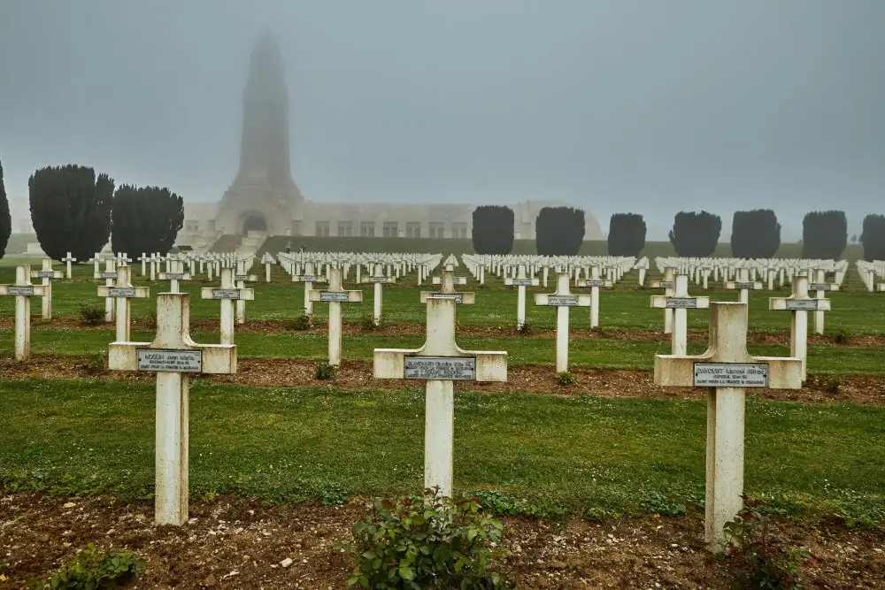 Croix blanches d'un cimetière militaire devant un monument aux morts dans la brume, symbole de la mémoire nationale.