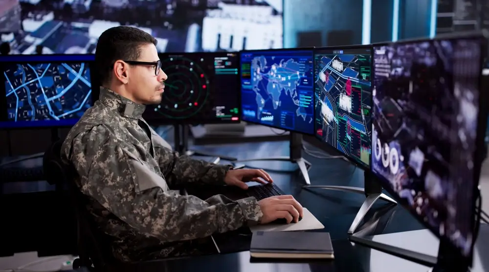 Soldat en uniforme avec insignes de grade travaillant sur des écrans tactiques dans un bureau de l'armée de Terre.