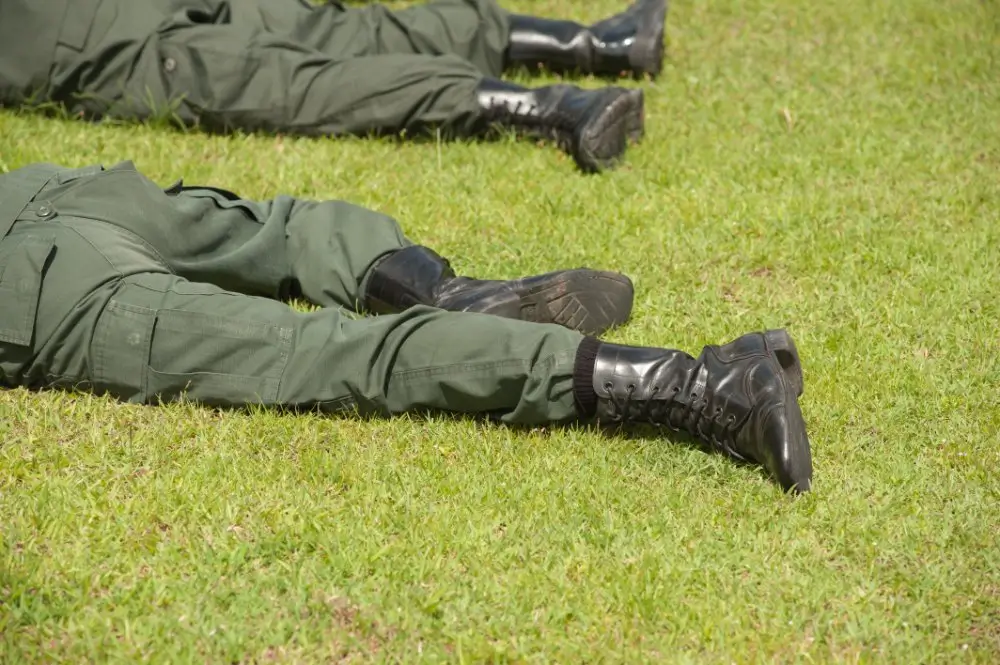 Soldats en treillis allongés au sol lors d'un exercice de manœuvre tactique sur un terrain militaire.