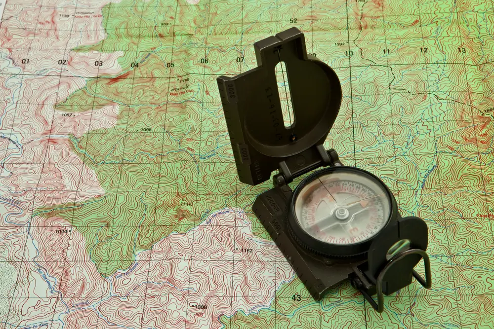 Boussole militaire ouverte sur une carte topographique à courbes de niveau pour l'orientation et la lecture de terrain.