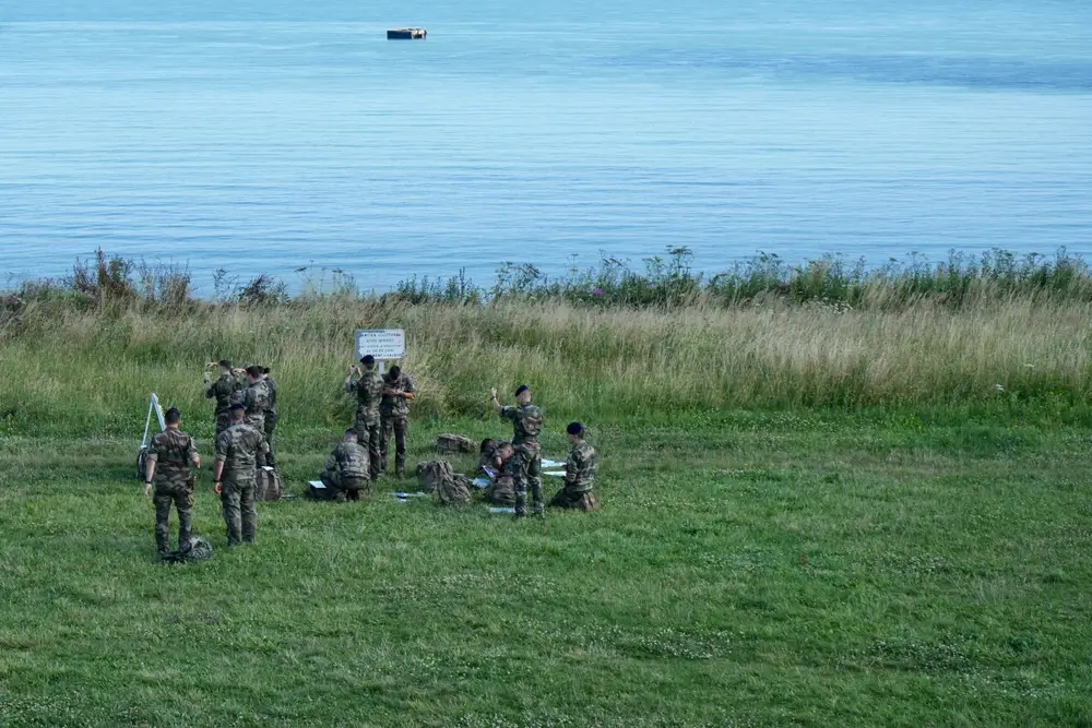 Soldats en entraînement militaire moderne sur une côte herbeuse, préparant une mission avec leur équipement opérationnel.